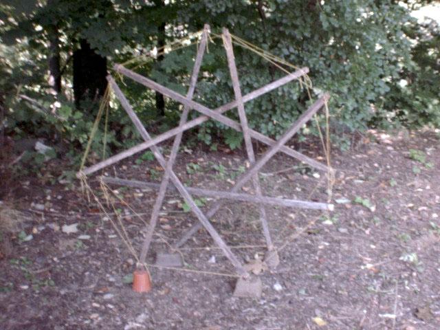 side (top?) view of seven-fold garden-stake-and-nylon-twine tensegrity prism standing on its side outdoors