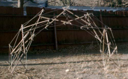 side view of stake and nylon twine arch against a red fence